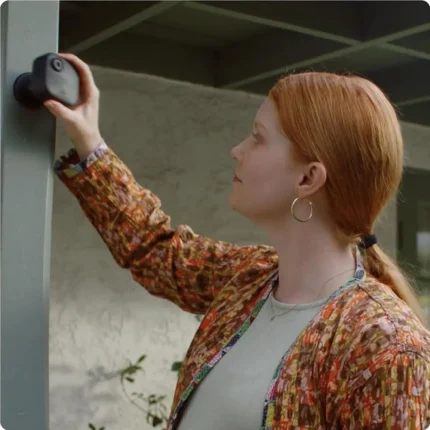 Mujer instalando una cámara Blink Outdoor 4 a pilas en un pilar exterior de madera sin usar cables.